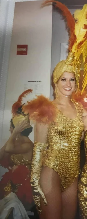 Tracey in a gold sequinned showgirl costume and feathered headdress, backstage.